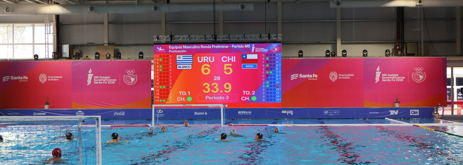Scoreboard LED de Prina sobre la pileta de waterpolo de los XIII Juegos Suramericanos Santa Fe 2026, con el partido Uruguay vs Chile en pantalla